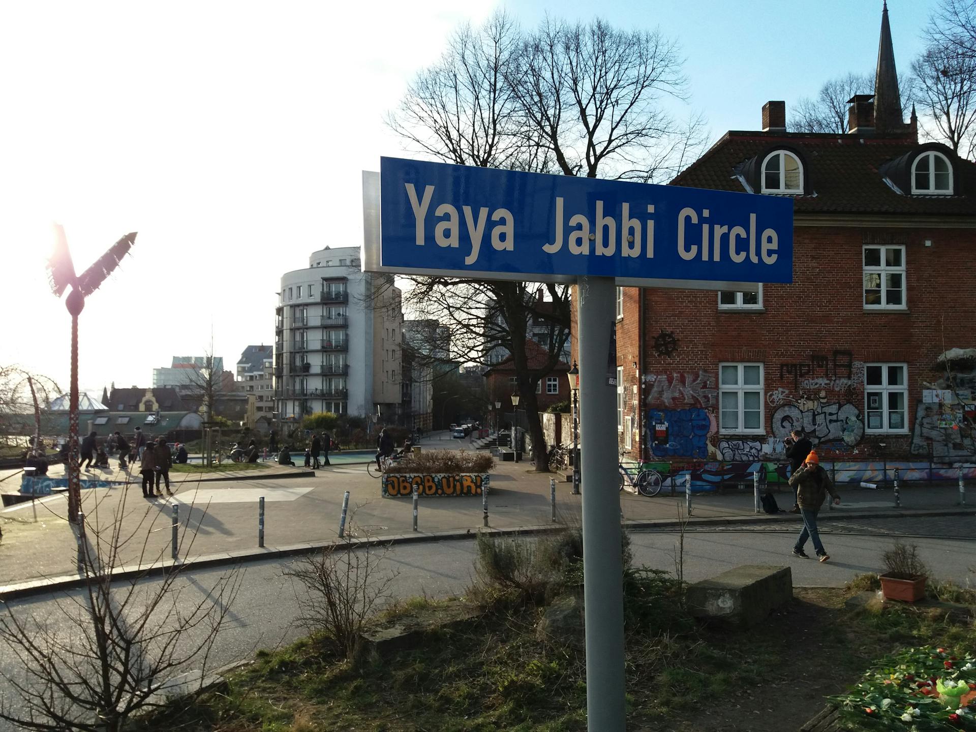 Close up photo of the 'Yaya Jabbi Circle'-street sign on a sunny day. Park Fiction in the background